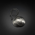 Pair of silver coin earrings on a dark background