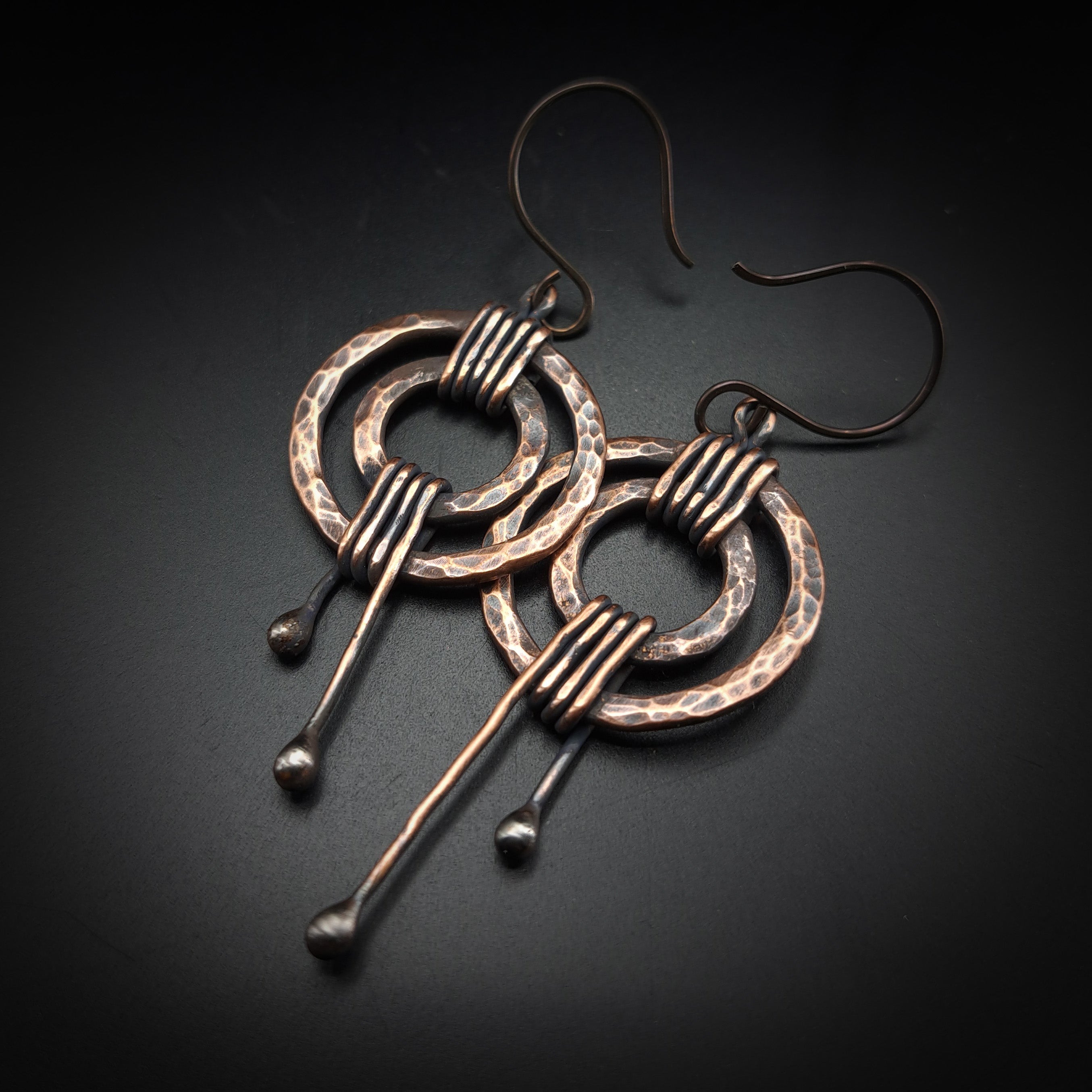Hammered copper double ring earrings flat lay, dark background — wire wrap detail close-up