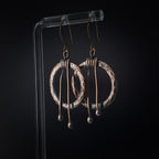 Hammered copper hoop earrings on acrylic stand, black background — wire wrap close-up