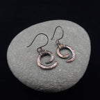 Hammered copper spiral earrings on river stone, dark background — Vortex