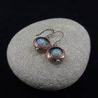 Copper ring earrings with aquamarine chalcedony on gray stone, black background — textured oxidized finish, RVSTICA