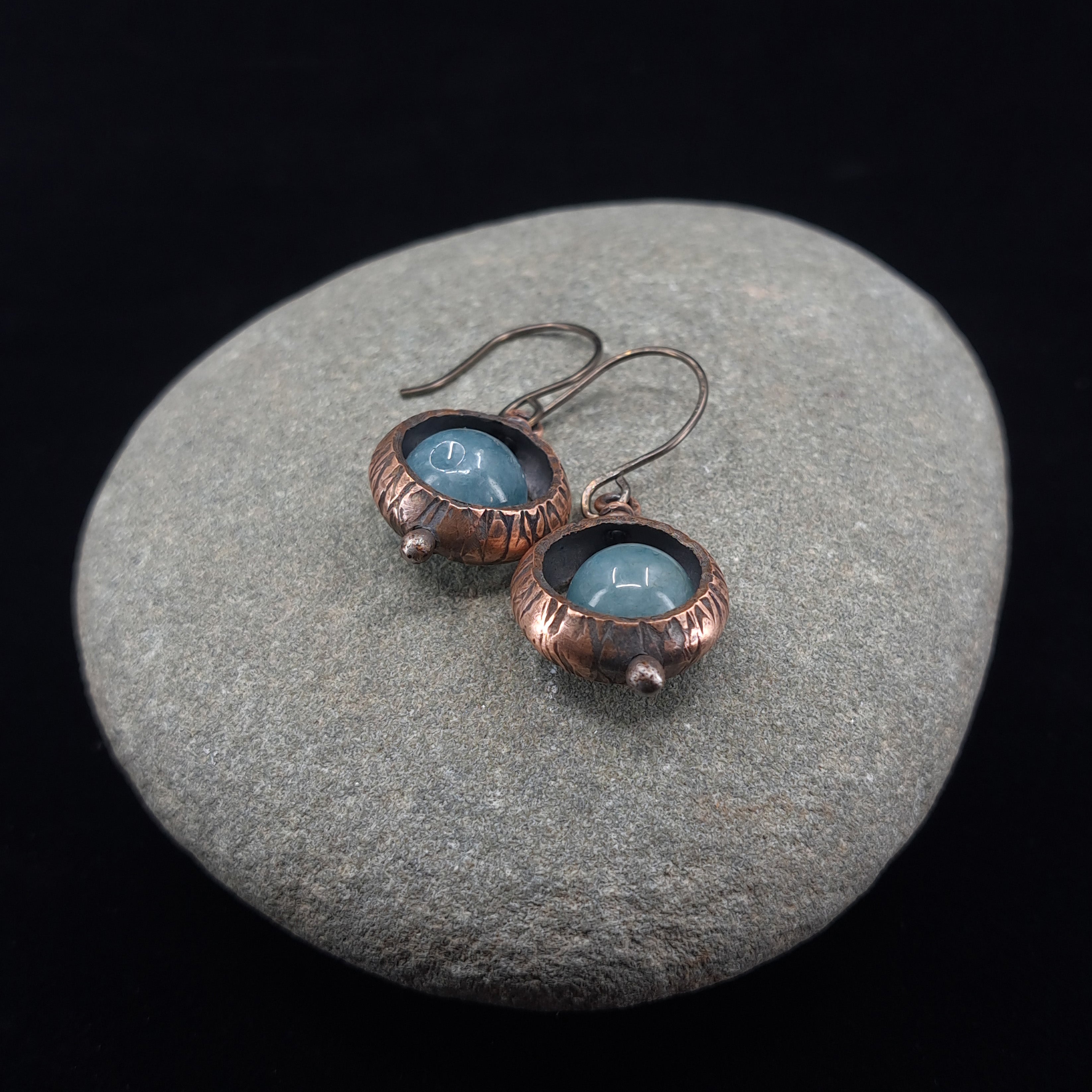 Copper ring earrings with aquamarine chalcedony on gray stone, black background — textured oxidized finish, RVSTICA