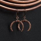 Lunar Horns earrings hanging on copper coil — black fabric background
