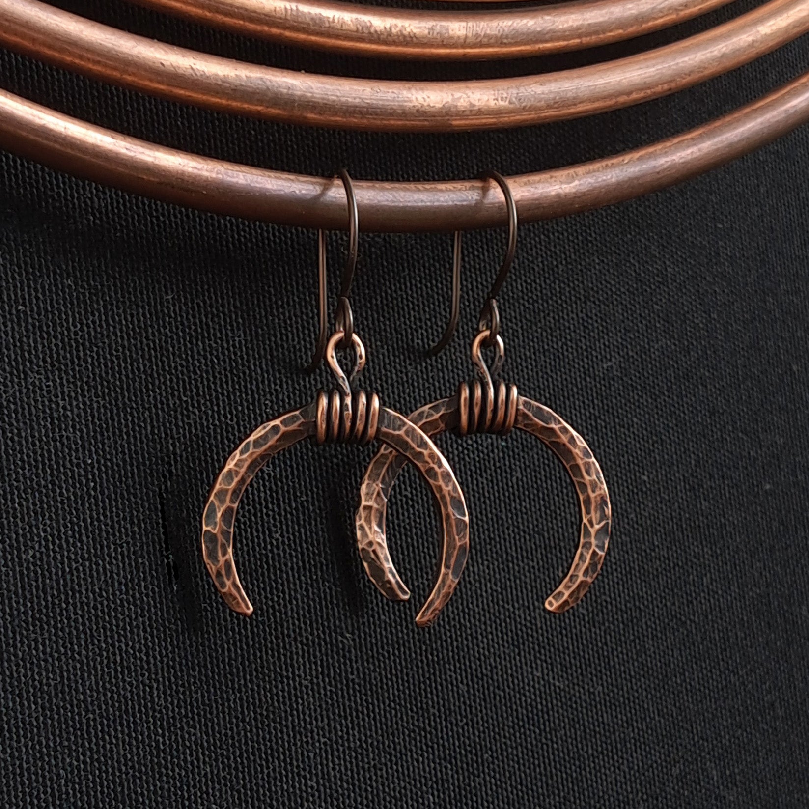 Lunar Horns earrings hanging on copper coil — black fabric background