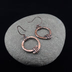 Copper open ring earrings on river stone, dark background — Torque