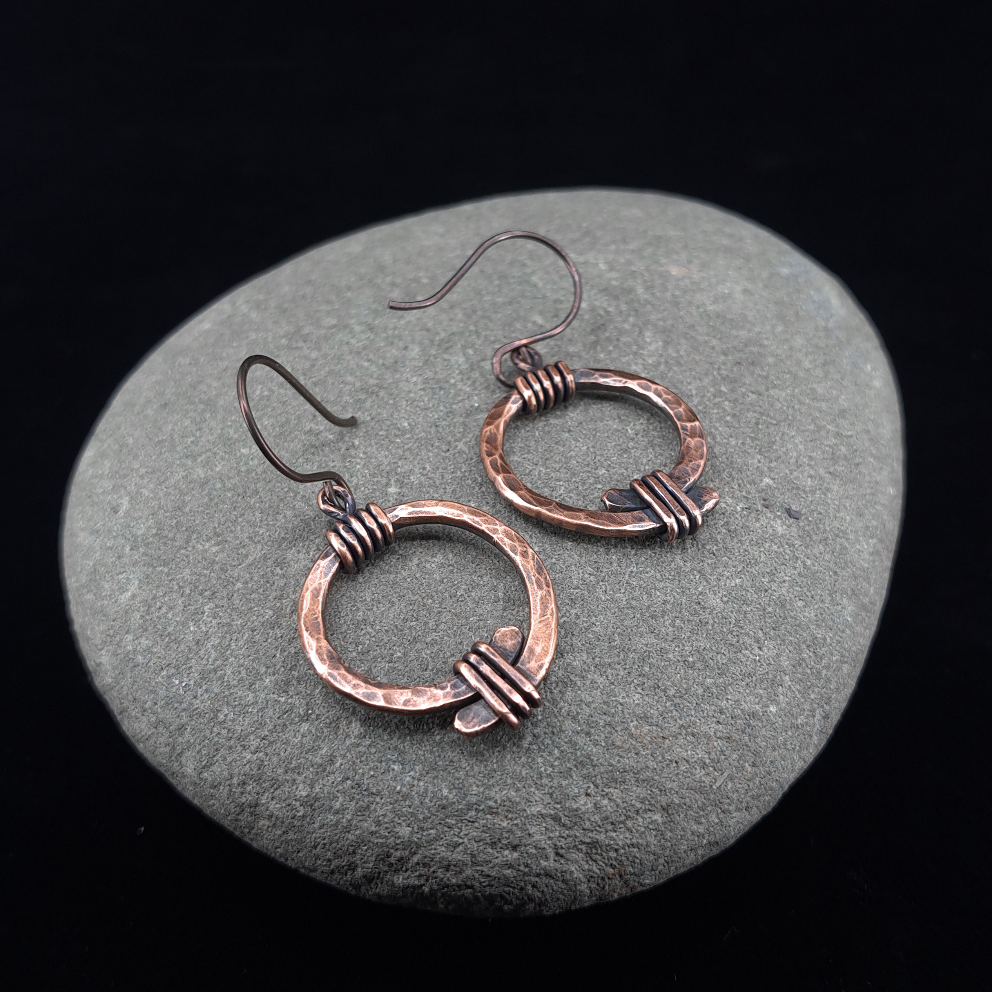 Copper open ring earrings on river stone, dark background — Torque