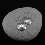 Shiny upcycled dime earrings on a grey stone background