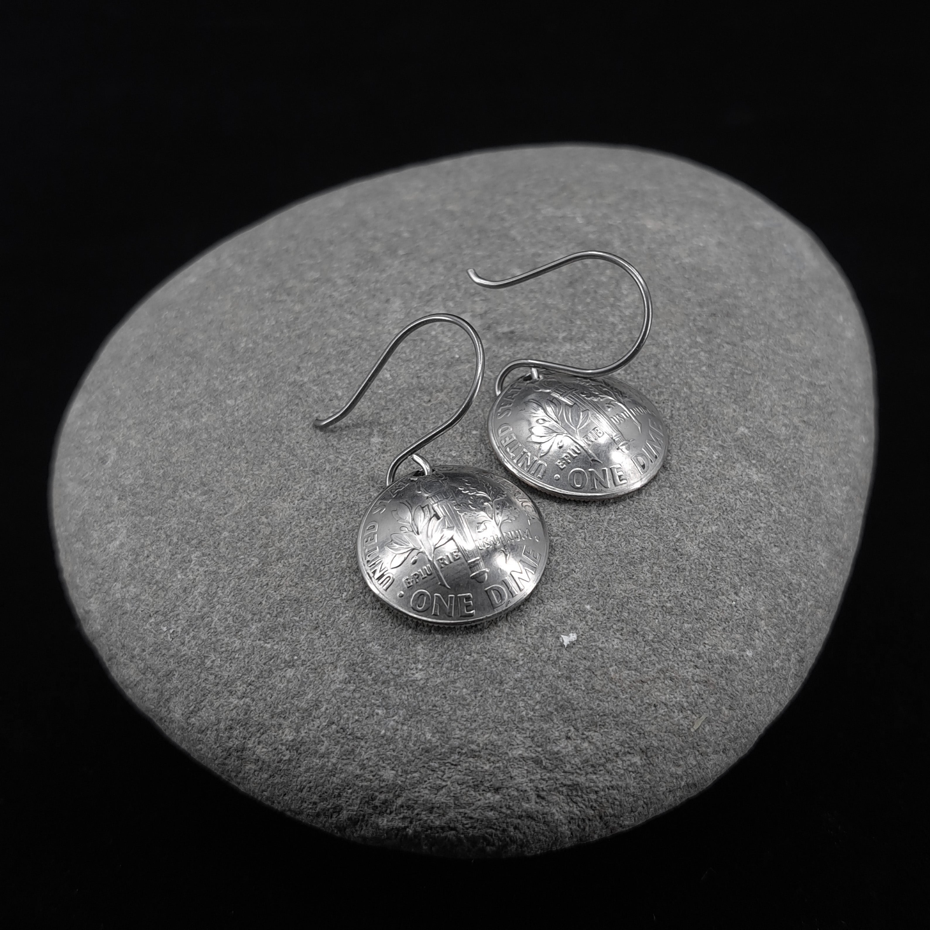 Shiny upcycled dime earrings on a grey stone background