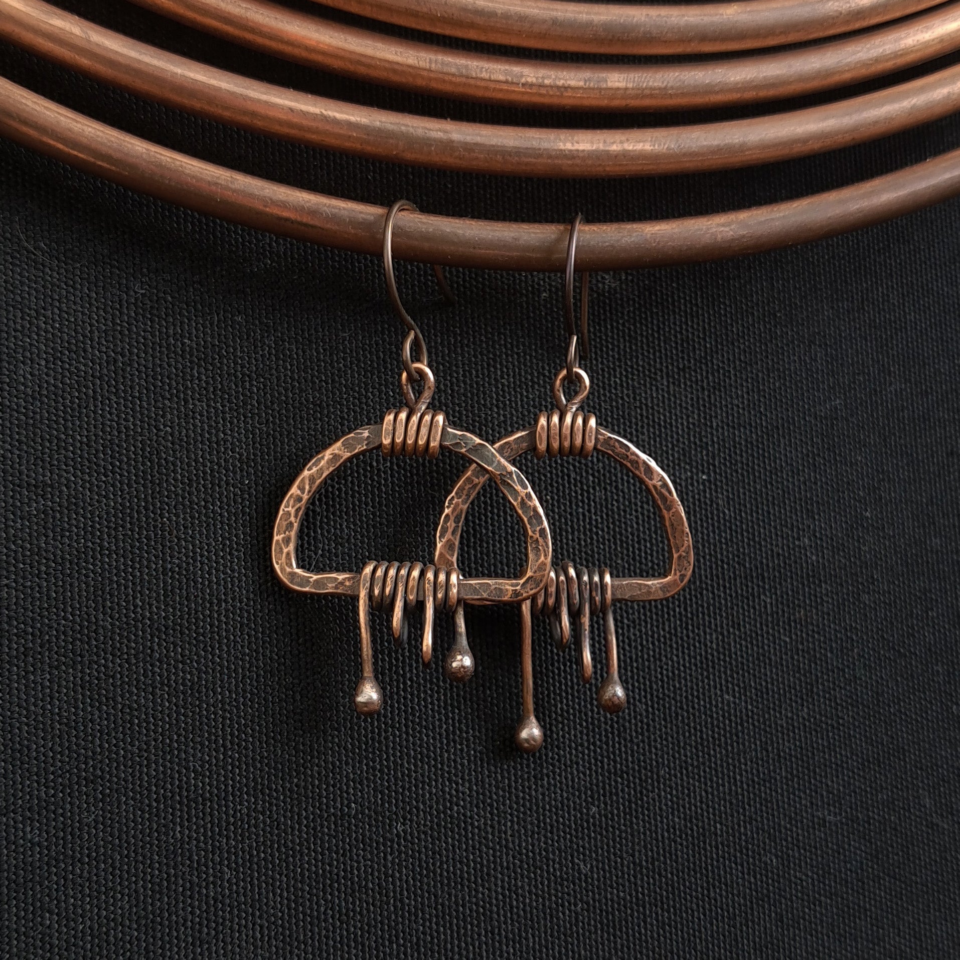 Earrings hanging on copper wire coil, dark fabric background — Nimbus Storm