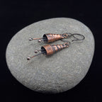 Copper spiral earrings on a gray stone, black background — handmade, RVSTICA