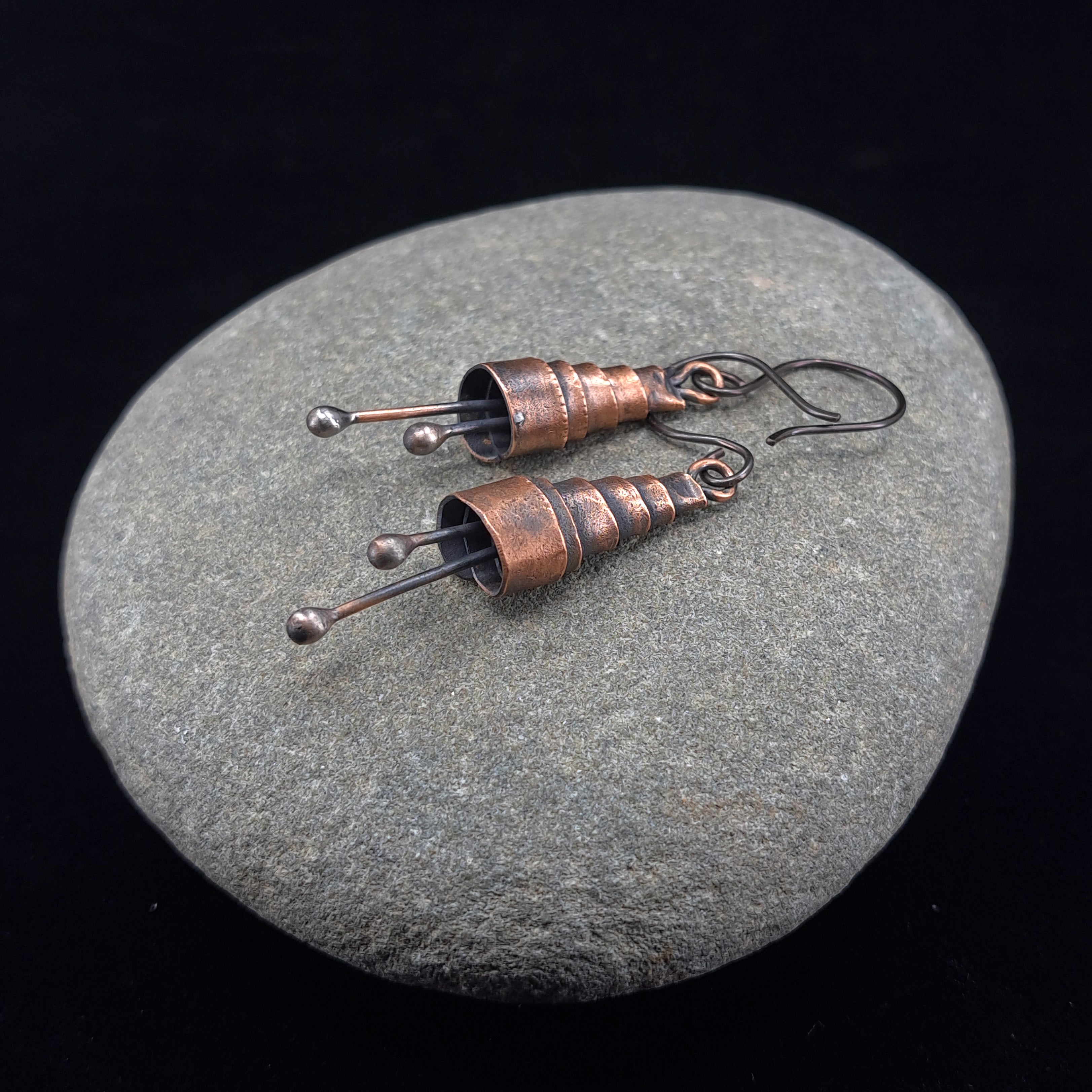 Copper spiral earrings on a gray stone, black background — handmade, RVSTICA