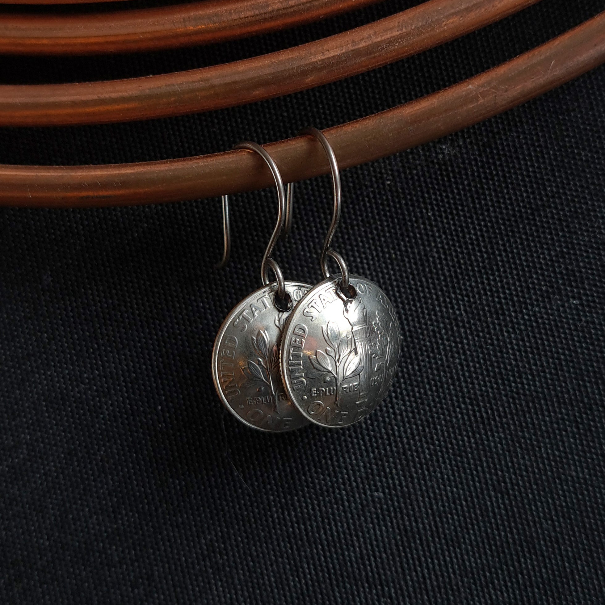 Vintage Currency dime earrings hanging on copper coil — dark fabric background