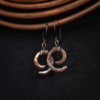Copper spiral earrings hanging on copper coil, dark fabric background — Vortex