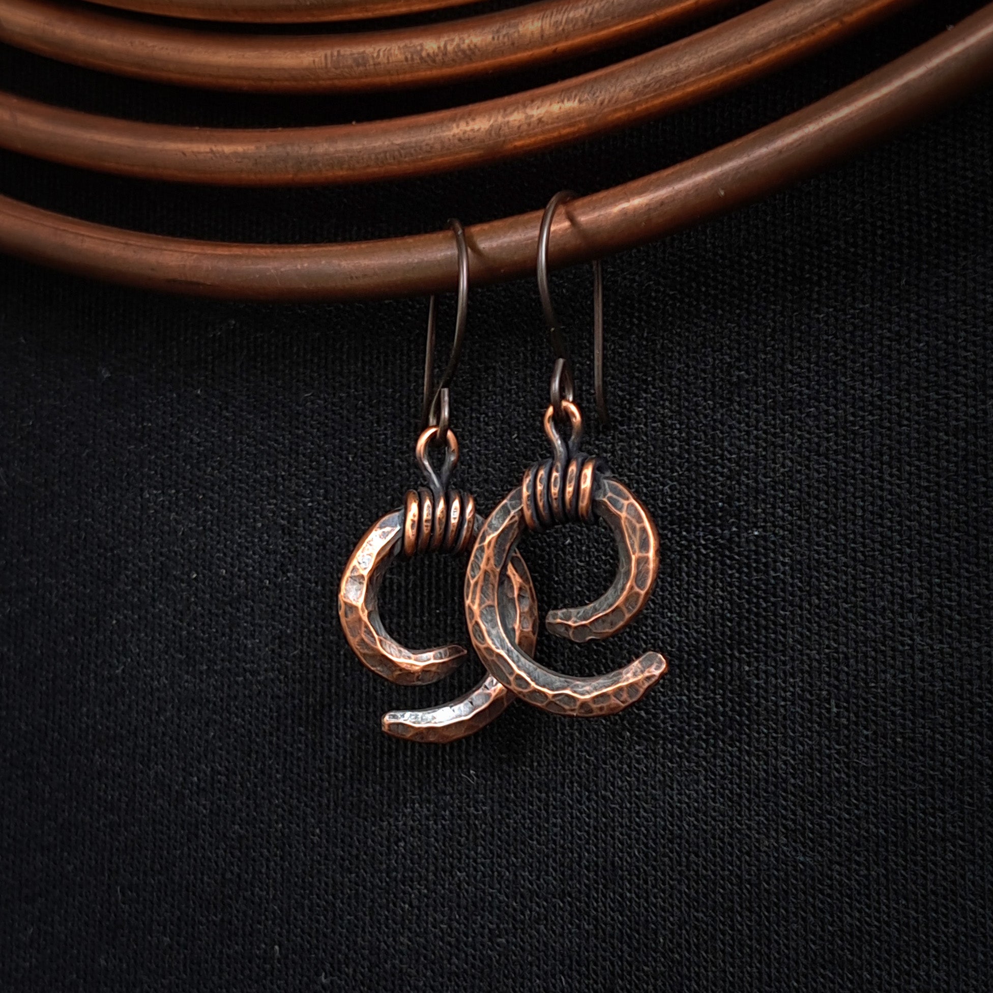 Copper spiral earrings hanging on copper coil, dark fabric background — Vortex