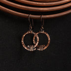 Copper open ring earrings on copper coil prop, dark fabric, warm tone — Torque