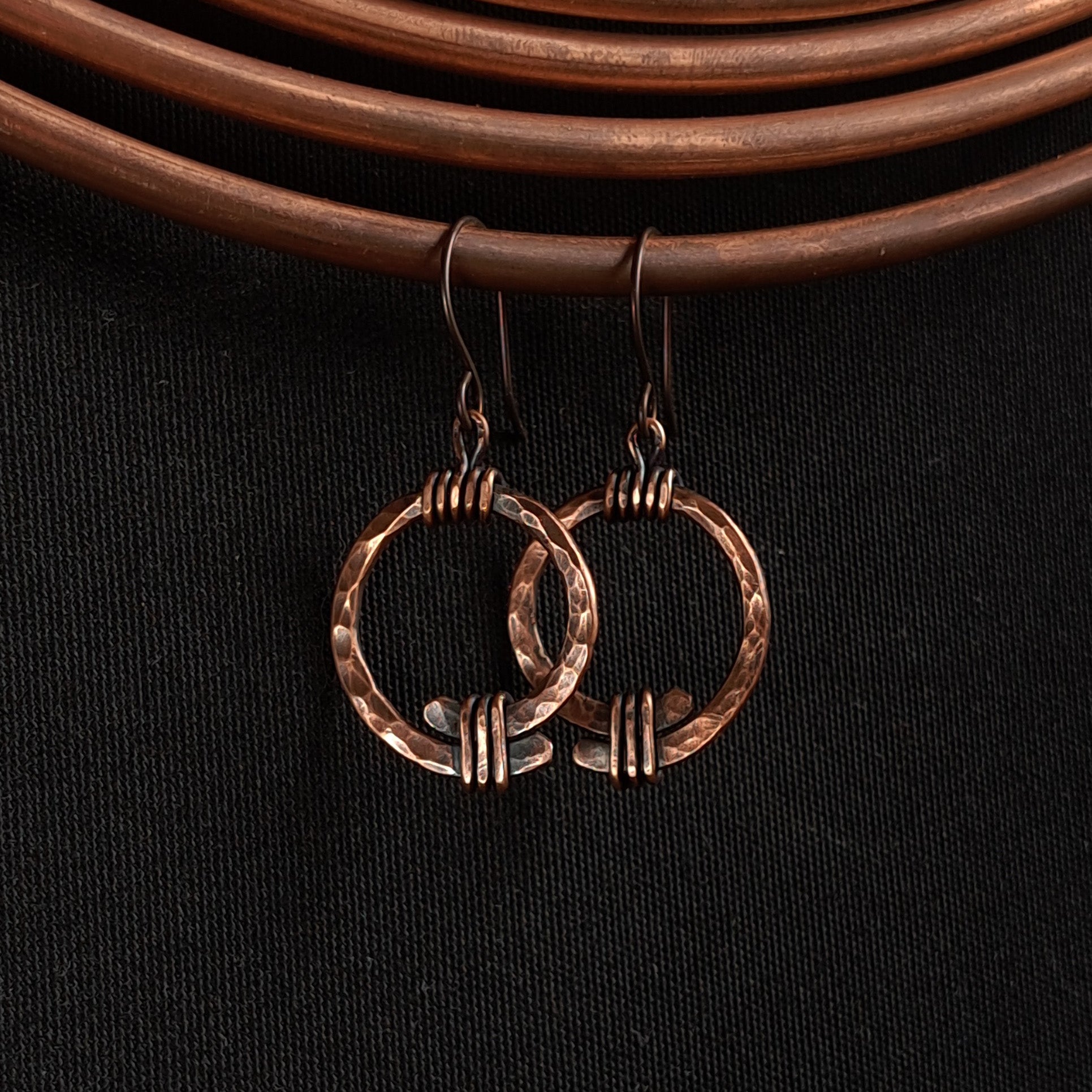 Copper open ring earrings on copper coil prop, dark fabric, warm tone — Torque