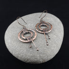 Hammered copper double ring earrings on gray stone, dark background — rustic patina, handmade