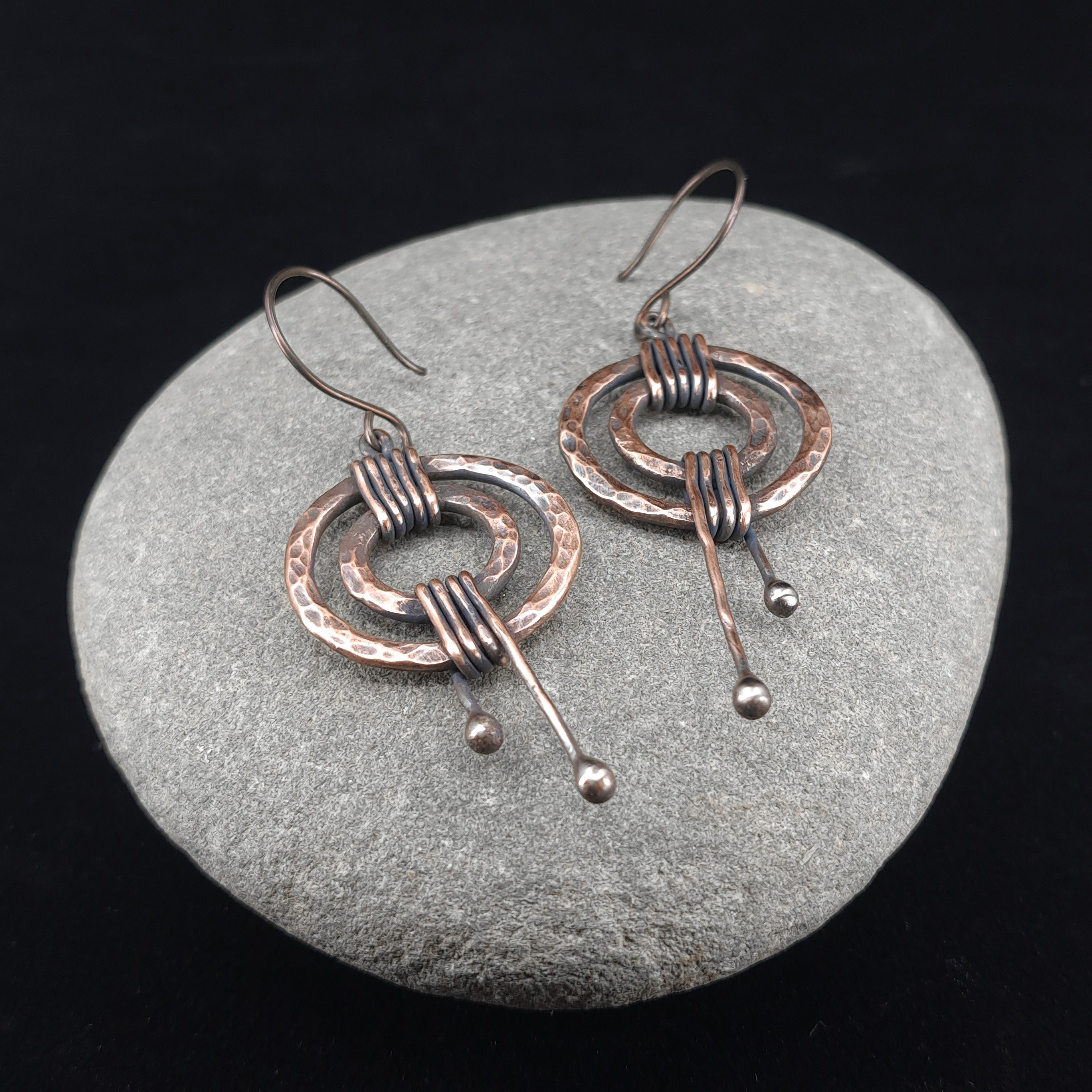 Hammered copper double ring earrings on gray stone, dark background — rustic patina, handmade