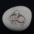 Hammered copper hoop earrings on gray stone — ball drop detail, niobium hooks.