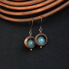 Copper ring earrings with aquamarine chalcedony on copper wire background — blue-green stone, dark background