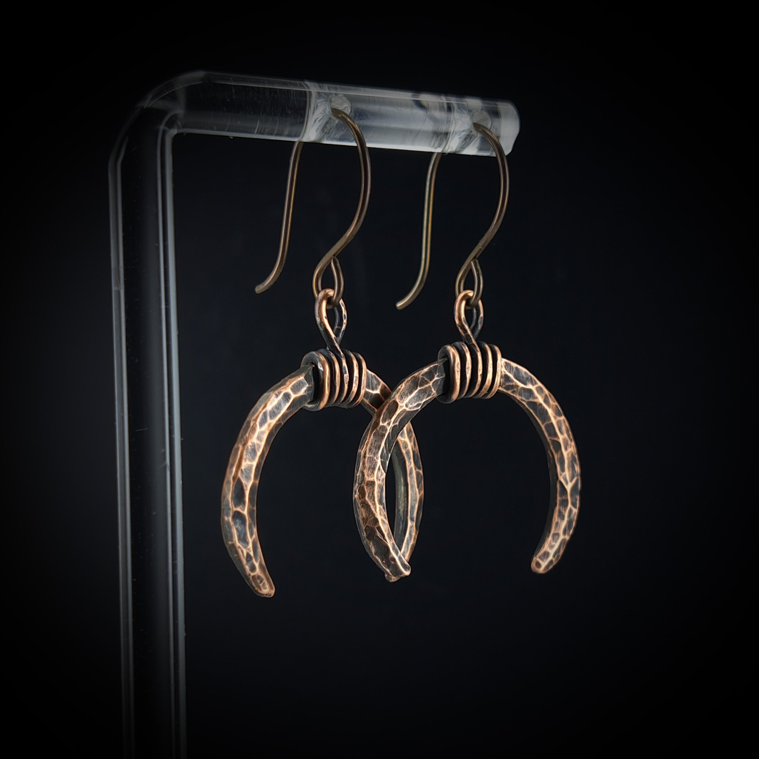 Lunar Horns earrings on acrylic stand — dark background, side view