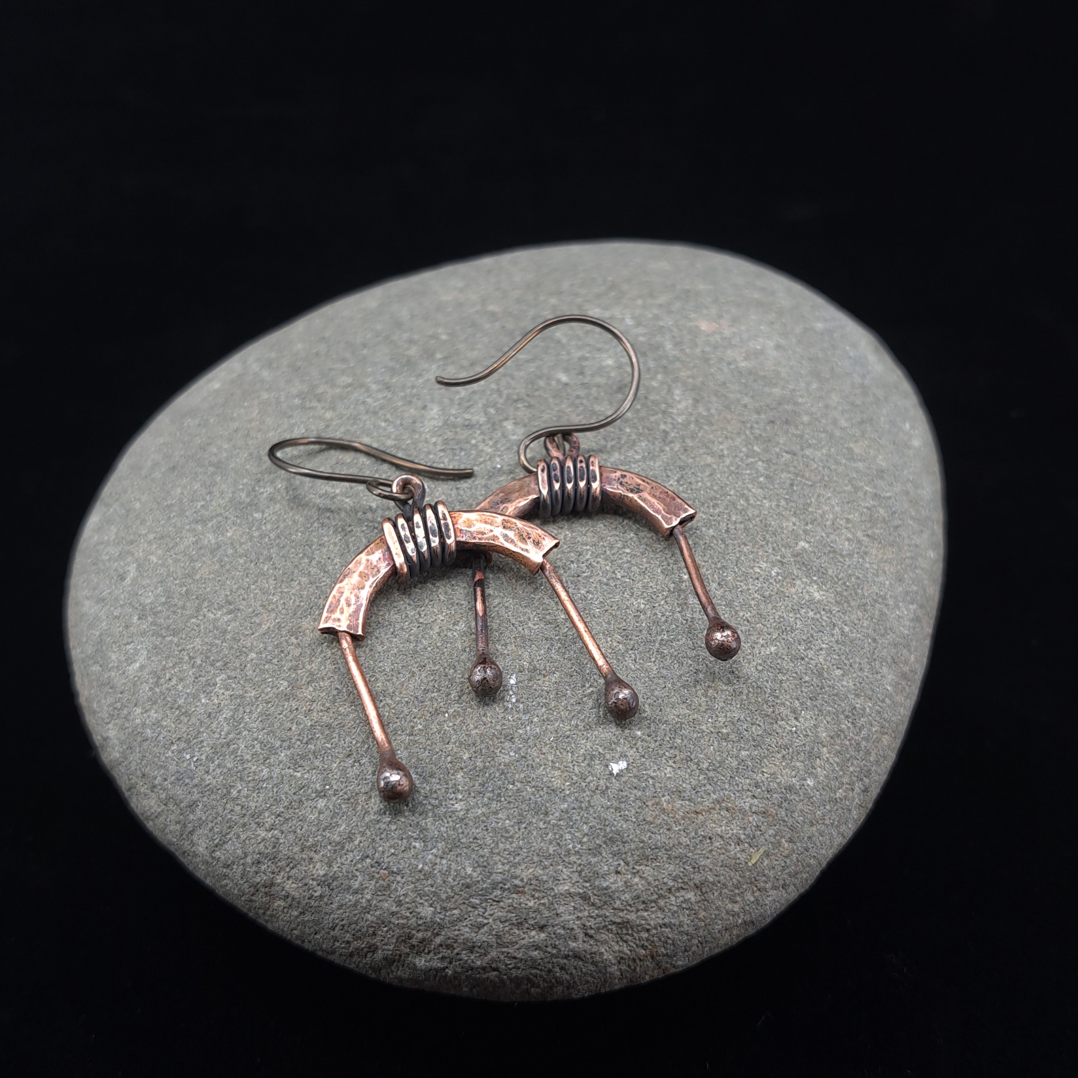 Copper arch earrings on natural river stone, dark background — U-Turn