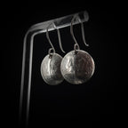 Upcycled coin dime earrings on acrylic stand — black background.
