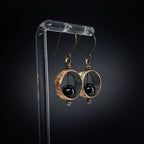 Copper & black onyx earrings on acrylic stand, dark background, front view — Meridian
