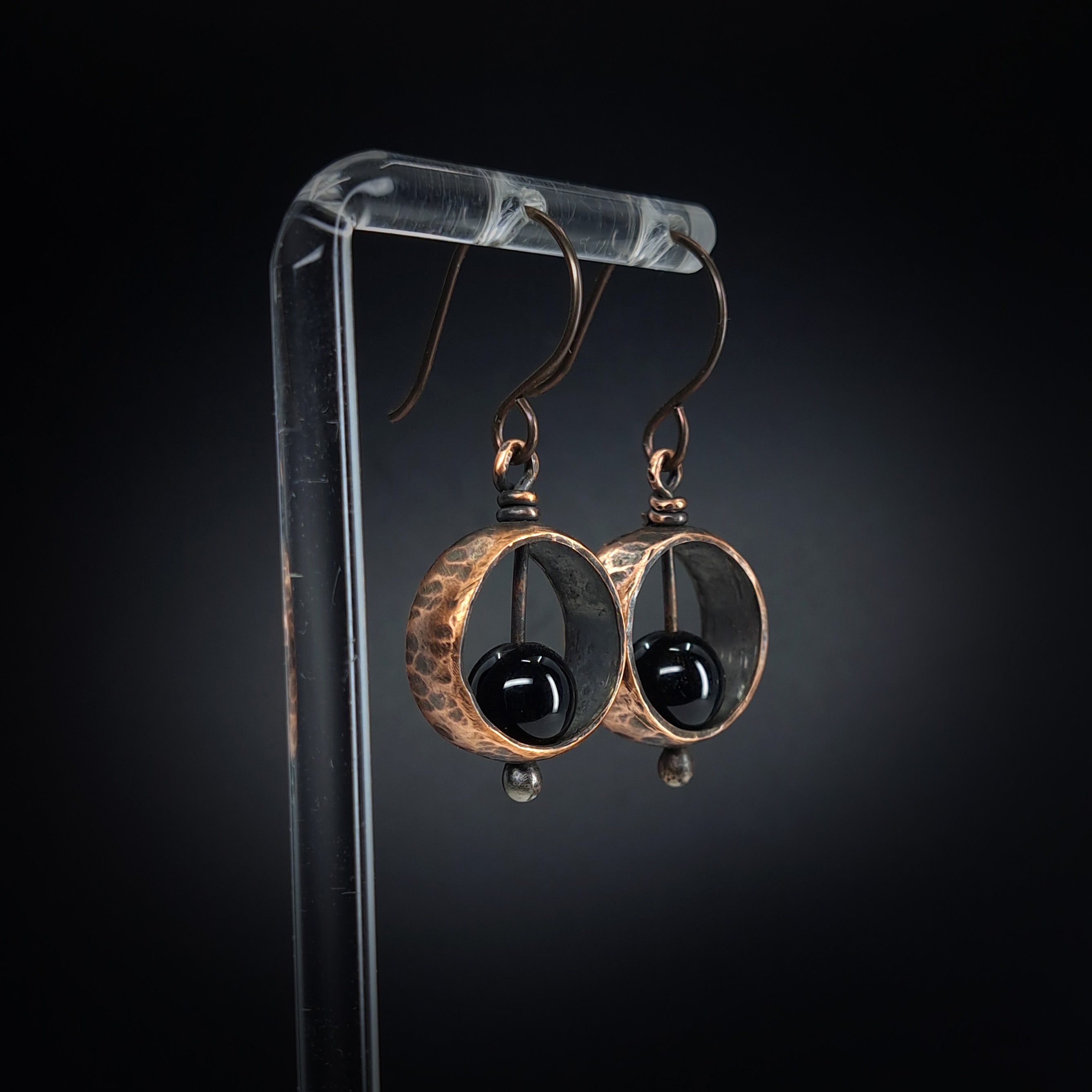 Copper & black onyx earrings on acrylic stand, dark background, front view — Meridian