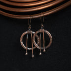 Hammered copper hoop earrings on copper wire background — dark oxidized texture