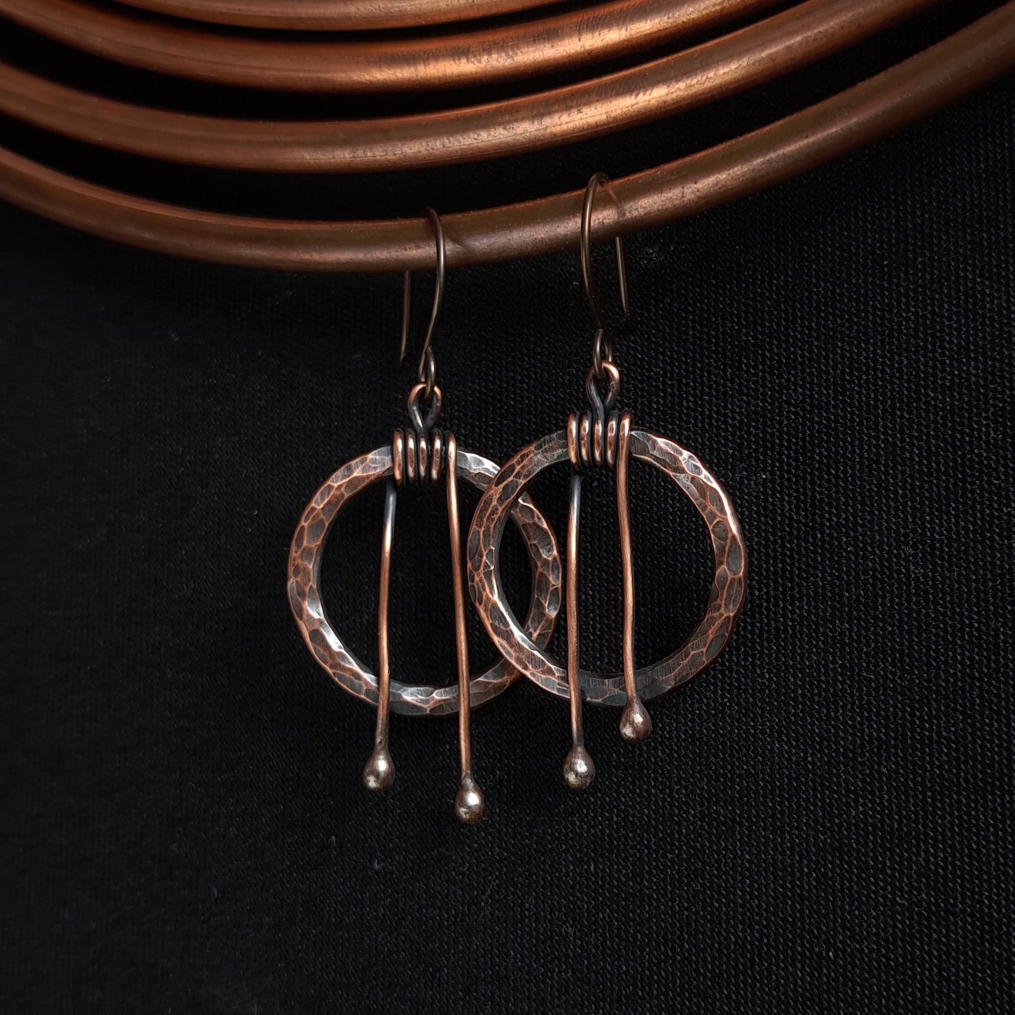 Hammered copper hoop earrings on copper wire background — dark oxidized texture