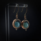 Copper ring earrings with aquamarine chalcedony on acrylic stand, black background — front view, oxidized copper