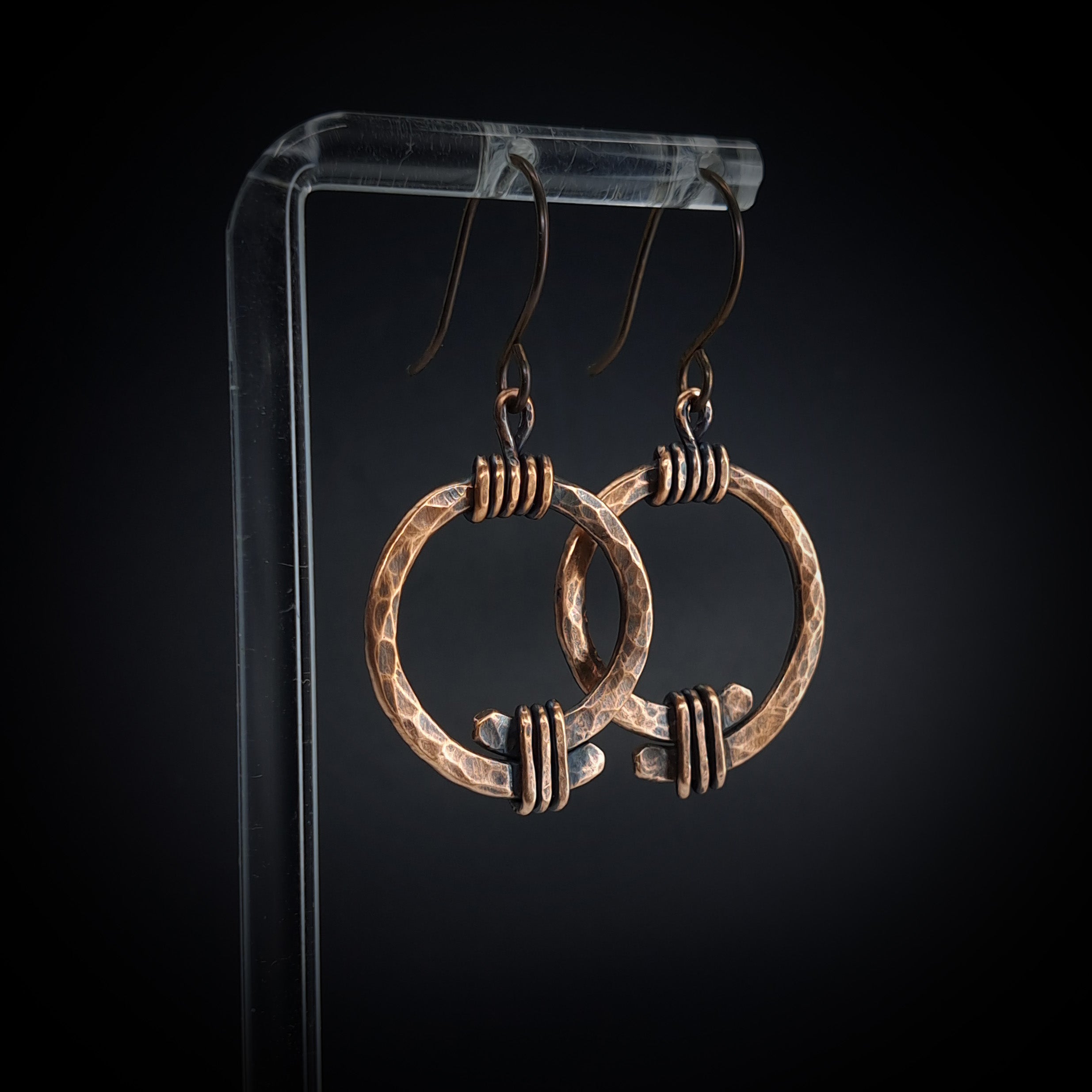 Hammered copper open ring earrings on acrylic stand, black background, front view — Torque