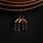 Copper arch earrings close-up showing coil wrap and fire-fused ball-tip drops — U-Turn