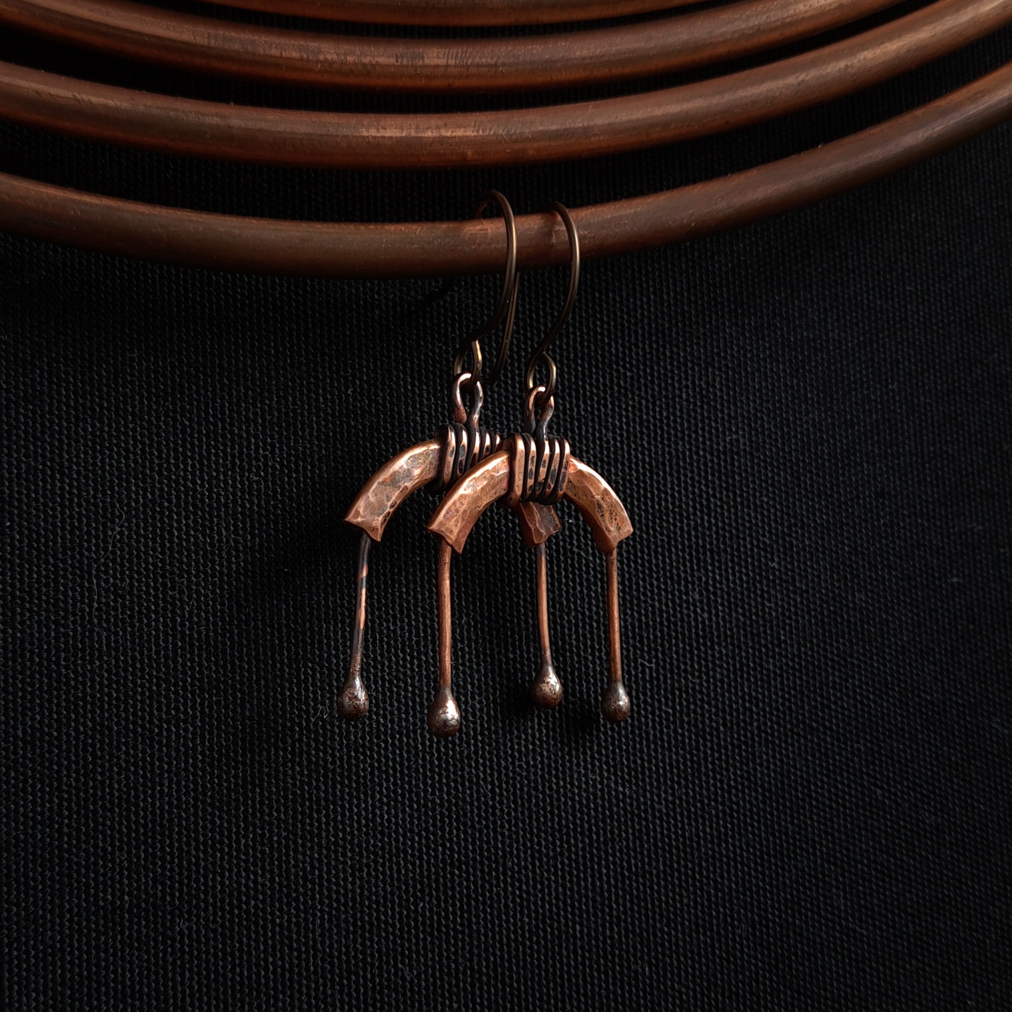 Copper arch earrings close-up showing coil wrap and fire-fused ball-tip drops — U-Turn