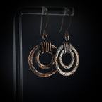 Hammered copper double hoop earrings on acrylic stand — dark background