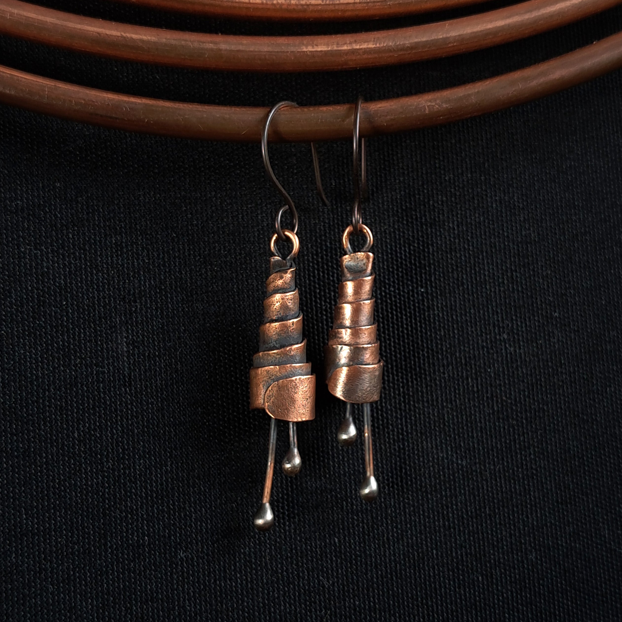 Copper spiral earrings hanging on copper wire, black background — oxidized finish