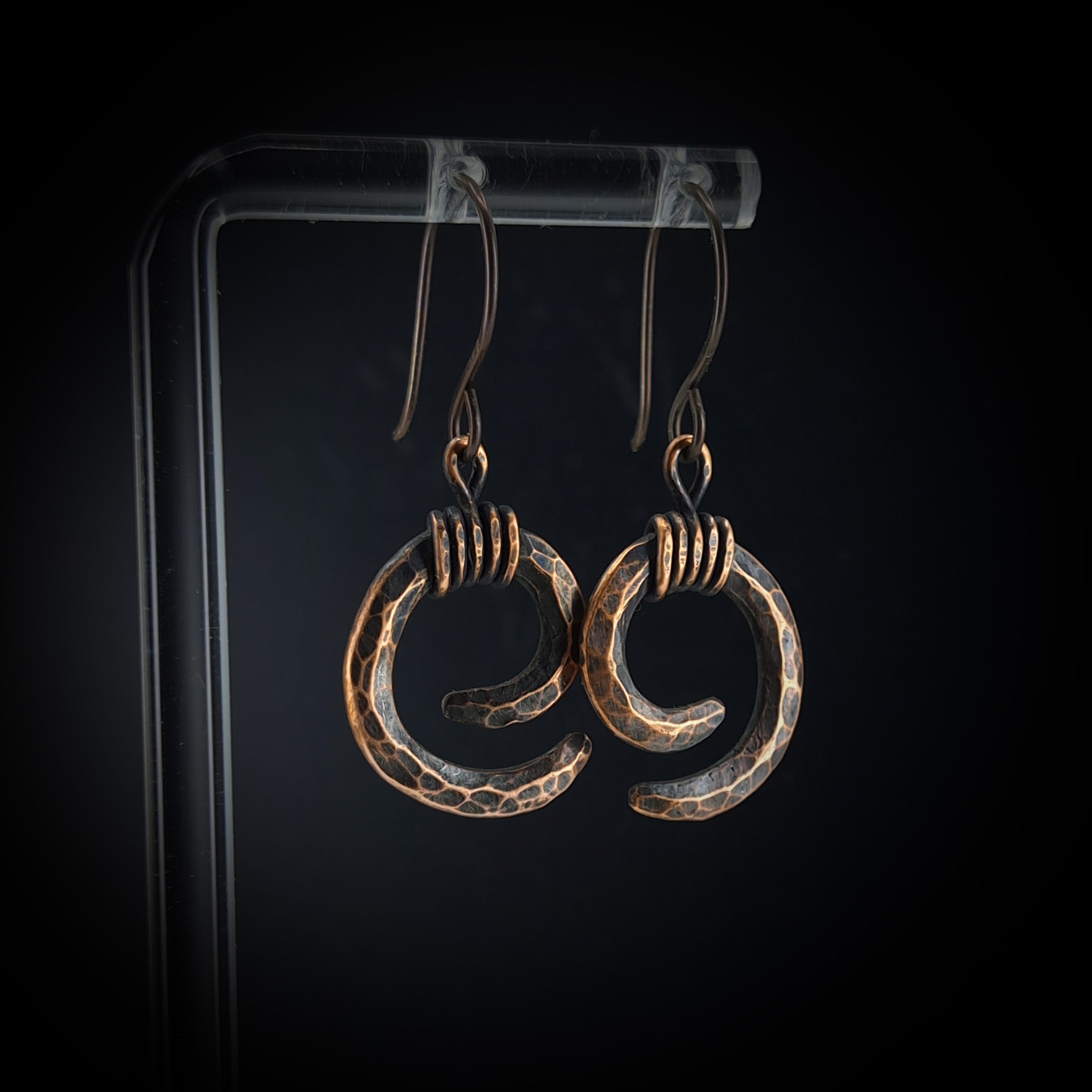 Copper spiral earrings on acrylic stand, dark background, warm light — Vortex