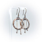 Hammered copper hoop earrings on acrylic stand, white background — side view