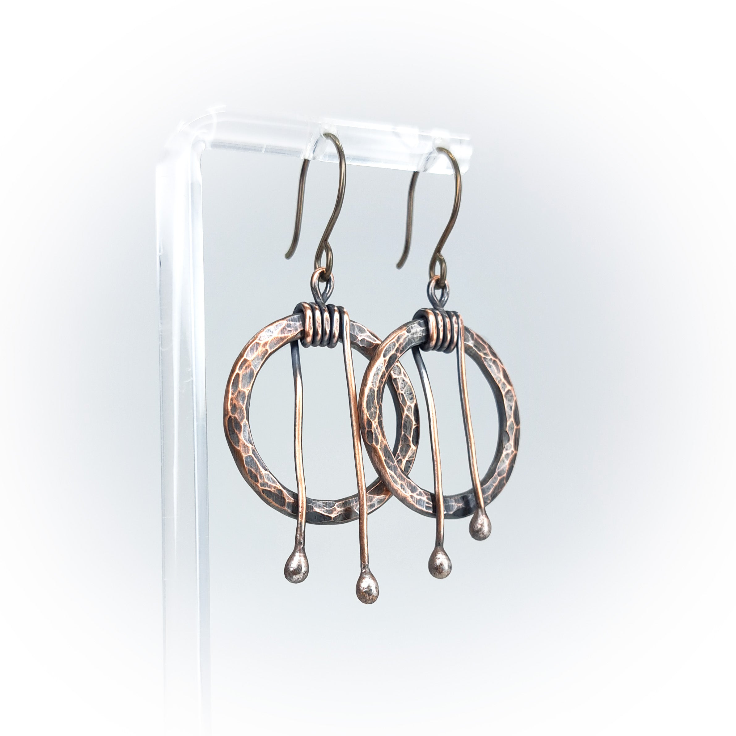 Hammered copper hoop earrings on acrylic stand, white background — side view