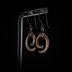 Copper spiral earrings on acrylic stand, dark background, side view — Vortex