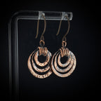 Pair of copper earrings on a clear stand against a black background