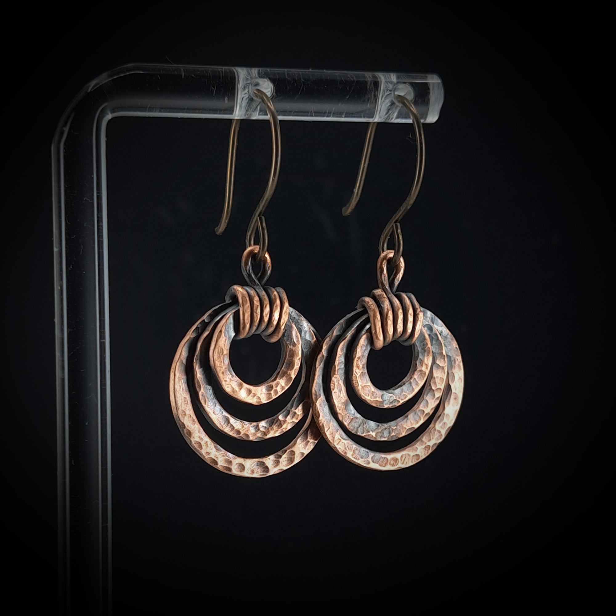 Pair of copper earrings on a clear stand against a black background
