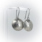 repurposed silver coin earrings on acrylic stand — white background, side view