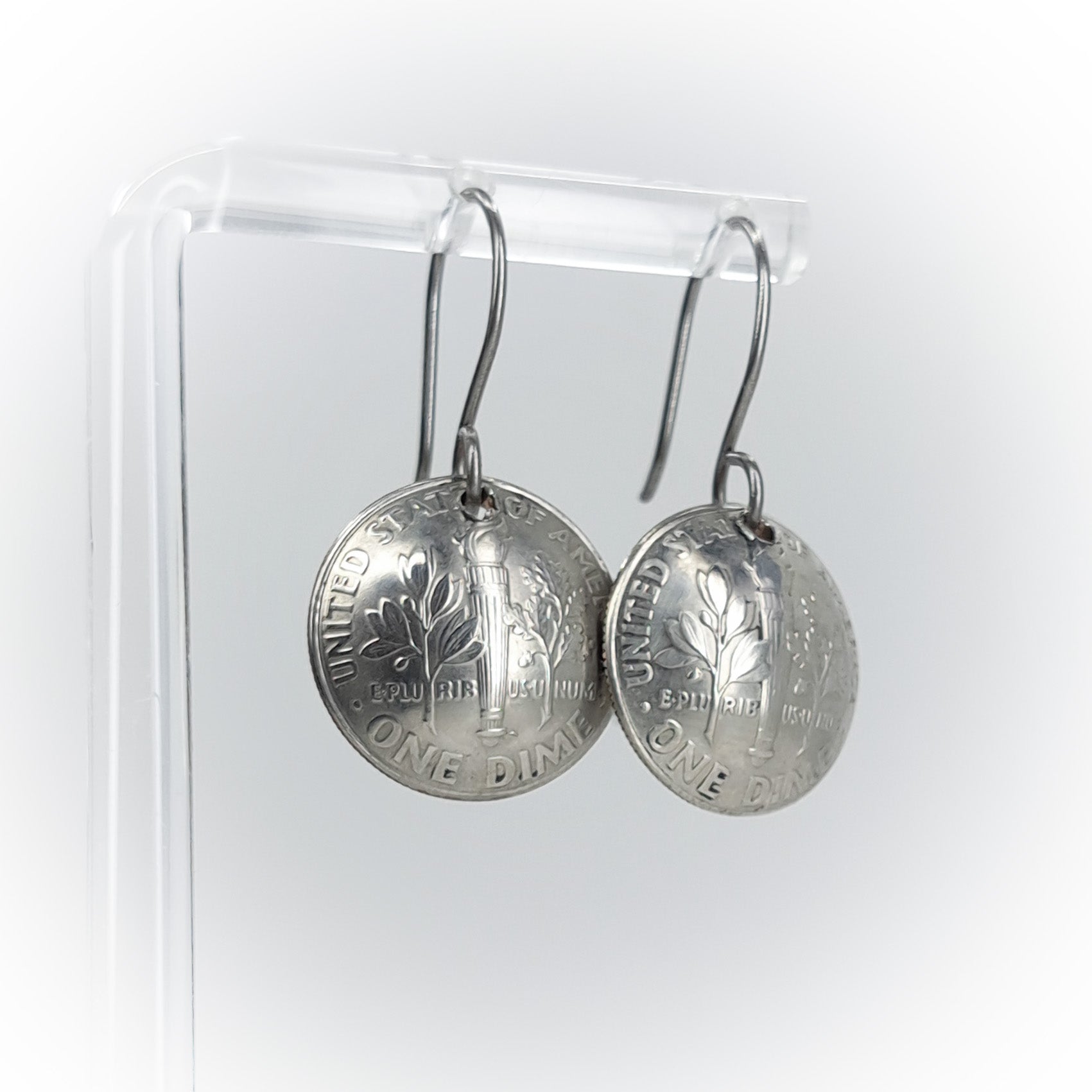 repurposed silver coin earrings on acrylic stand — white background, side view