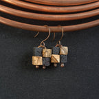 Terra Mosaic earrings hanging from copper coil — dark fabric background