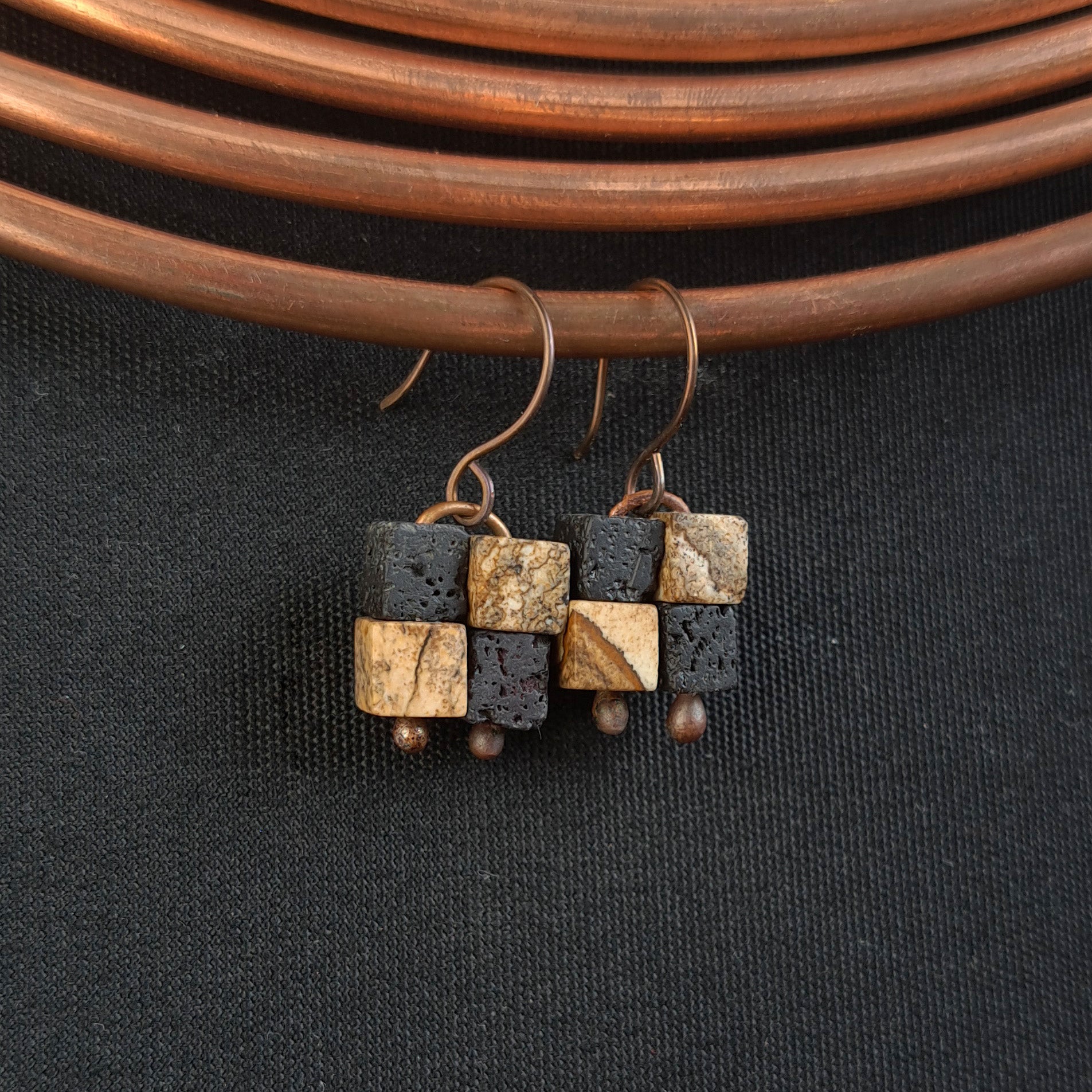 Terra Mosaic earrings hanging from copper coil — dark fabric background