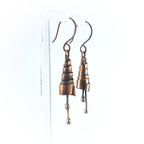 Copper spiral earrings on acrylic stand, white background — side view