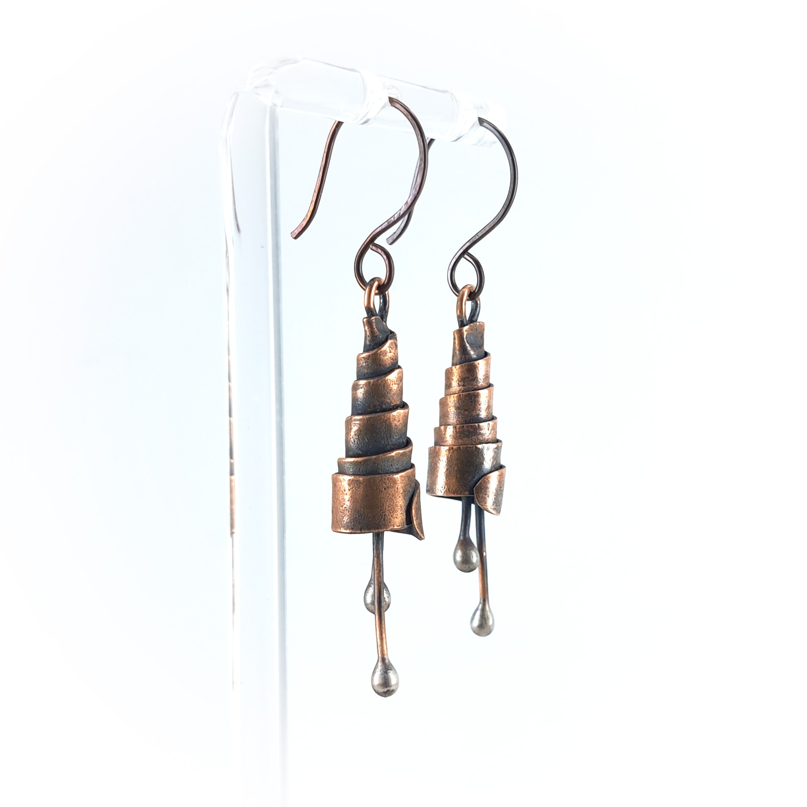 Copper spiral earrings on acrylic stand, white background — side view