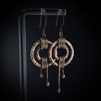 Hammered copper double ring earrings on black acrylic stand — oxidized finish, side view